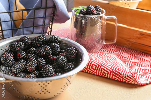 Colander and glass cup with fresh blackberries on orange background