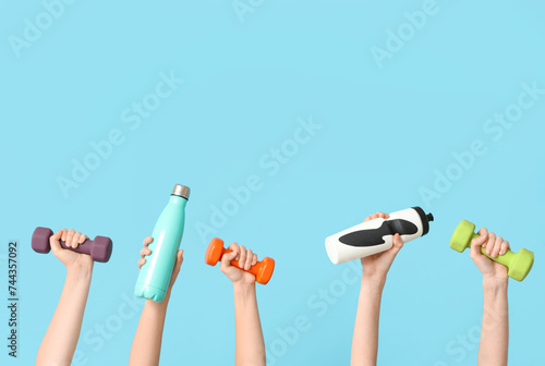 Female hands with dumbbells and bottles of water on color background
