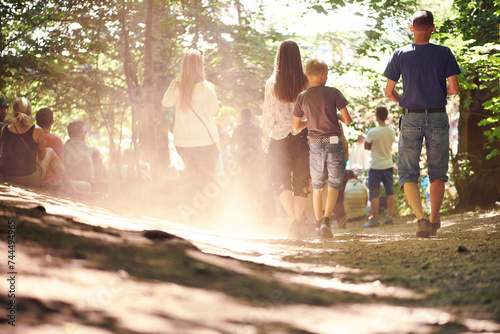 Festival, party and family walking in forest outdoor together for event, celebration or social gathering. Mother, father and children in nature, park or woods for summer entertainment from back