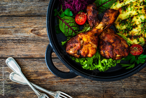 Baked chicken drumsticks with red cabbage and potato puree on wooden table 