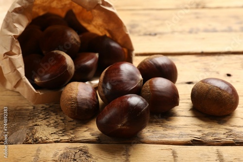 Sweet fresh edible chestnuts in paper bag on wooden table, closeup