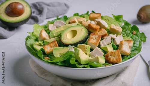 Caesar salad with lettuce, chicken, avocado and croutons on light table.