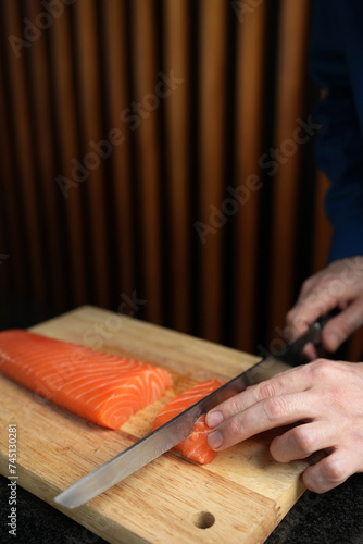 Chief hands cut salmon fillet with knife on wooden table