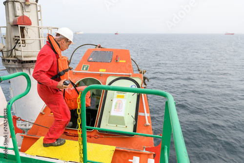 Seaman wearing lifejacket with vhf radio on Muster station. Abandon ship drill. Free fall boat. Cargo vessel.