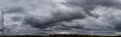 Panoramafoto einer geschlossenen, grauen Wolkendecke mit Gewitter- und Haufenwolken in Unteransicht