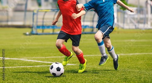 Two soccer players chase a soccer ball in a duel. Boys play soccer match on the grass pitch. Football academy players compete in school tournament. Youth footballers running and kicking ball