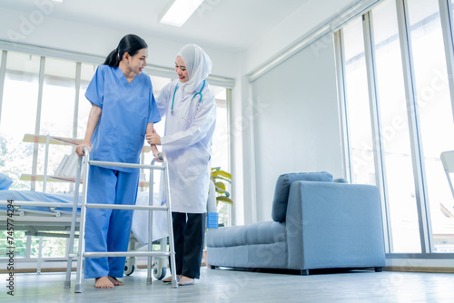 Healthcare, A Muslim Female doctor help a patient who is doing physical therapy and is practicing walking with a walking stick in the hospital.