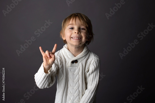 Cute little toddler boy, showing gesture in sign language on gray background, isolated image, child showing hand sings