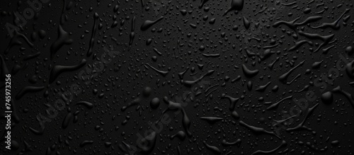 Numerous water drops are scattered across a black, plastic grainy abstract background. The drops reflect light, creating a striking contrast against the dark surface.