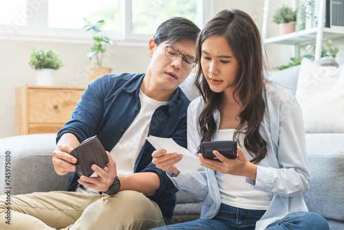 Stressed financial owe asian young couple love sitting stressed and confused by hand hold wallet calculate expense from invoice , no money to pay, mortgage or loan. Debt, bankrupt or bankruptcy people
