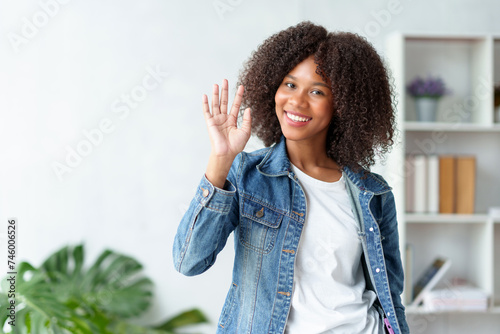 Smiling woman waving in casual attire. Modern lifestyle and friendly gesture concept.