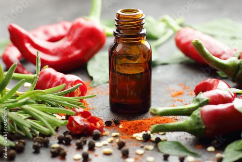 Red chili pepper oil, tincture, extract or vinegar with fresh vegetables and leaves on black table, closeup, copy space, organic spicy food, hair and body healthy care concept