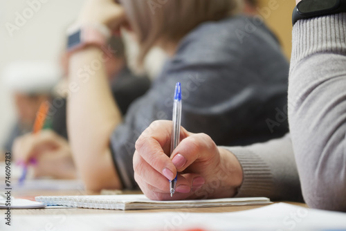 An adult woman with a fountain pen sits next to colleagues and writes in a notebook during a meeting or professional development training session.Photo. No face. Selective focus