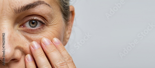 Cropped woman face with fingers under eye with wrinkles showing aging
