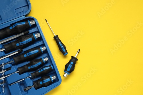 Set of screwdrivers and toolbox on yellow table, flat lay. Space for text