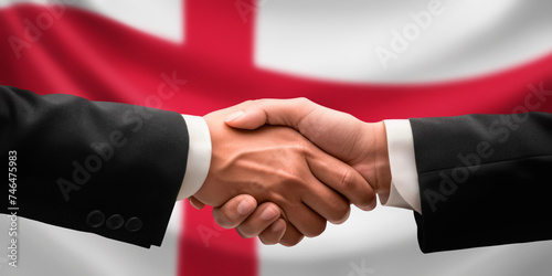 Businessman, diplomat in suits clasp hands for handshake over England flag, agree on united success in trade, diplomacy, cooperation, negotiation, support, teamwork in commerce, gesture of greeting