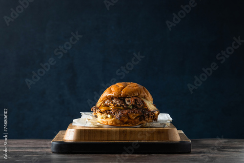 Deliciosa hamburguesa con doble carne aplastada, doble queso sobre tabla de cocina en una mesa de madera rústica en un fondo azul