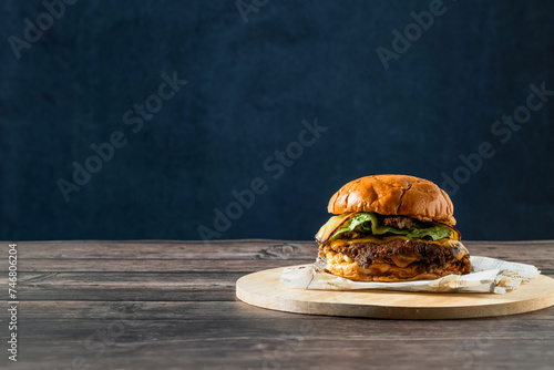 Deliciosa hamburguesa con doble carne aplastada, doble queso sobre tabla de cocina en una mesa de madera rústica en un fondo azul