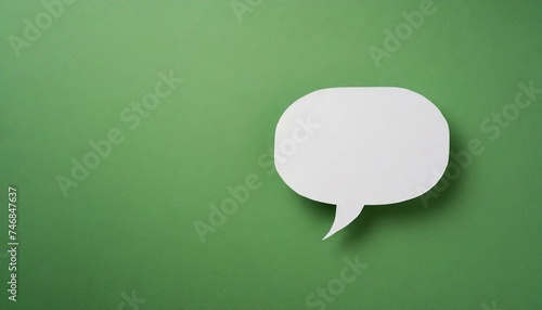 White paper cut out speech bubble shape set on green paper background.