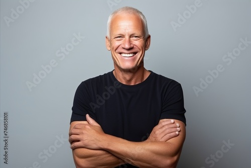 Portrait of a happy senior man with arms crossed against grey background