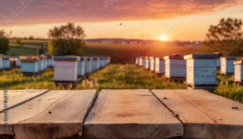 Empty wooden table top for product display. In the background, a blurred background of a small apiary at sunset