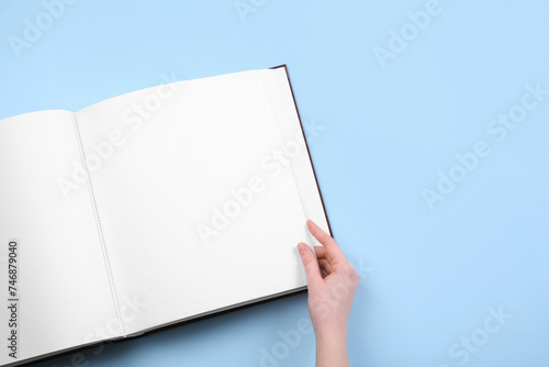 Woman with open photo album at light blue background, top view. Space for text