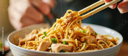 A person is enjoying Chinese noodles with chopsticks from a bowl, savoring the al dente rice noodles in the dish.