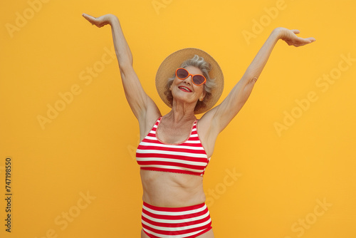 Cool funky elderly Latin American woman dressed striped red swimsuit dancing having fun isolated yellow color background