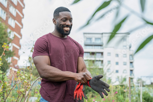Smiling man putting on gloves in urban vegetable garden
