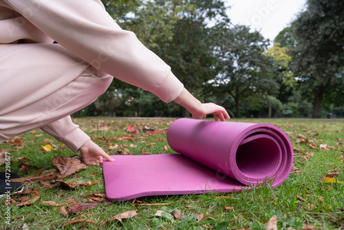 Close-up of woman unrolling yoga mat on grass in park