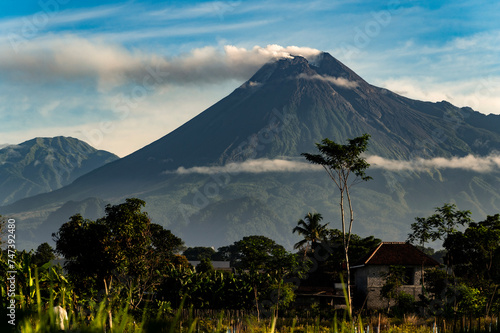 Beautiful Merapi volcano landscape view with tropical green trees foreground and cloudy blue sky background