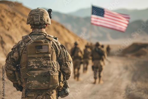 U.S. troops in the middle of their mission, walking through the field with their equipment and the American flag