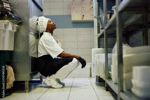 Exhausted black female cook in kitchen in restaurant.