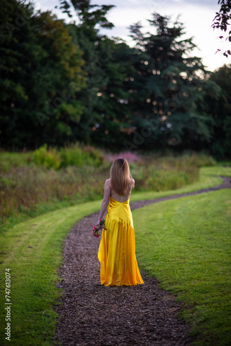 girl walking in a park with yellow dress and bare back with red roses