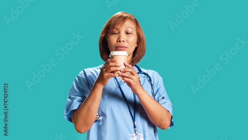 BIPOC nurse tasting instant coffee while at work, surprised by unexpected aroma. Close up shot of hospital employee drinking hot beverage with unusual aftertaste, isolated over studio background