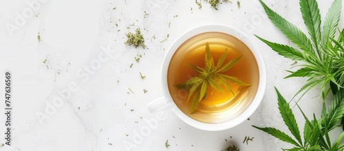 A cup of hemp tea with a marijuana leaf floating in it, placed on a white marble floor. The image captures the combination of cannabis and tea in a simple yet intriguing composition.