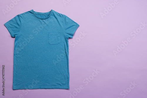 A plain blue t-shirt is laid out on a purple background, with copy space