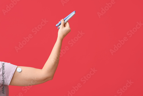Woman's hand with lancet pens and glucose sensor on red background. Diabetes concept