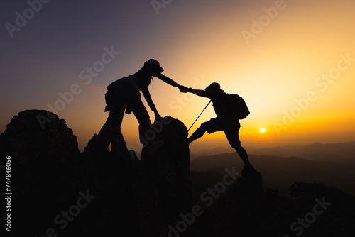 silhouette of People helping each other hike up a mountain at sunrise. Giving a helping hand, and active fit lifestyle concept. help and success concept, Leadership Concept, teamwork.