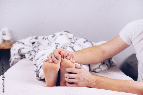 Bare feet of a child. The child is sleeping in bed. Legs look from under the blankets. Legs and heel. Hands tickle