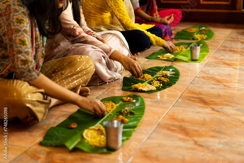 Traditional South Indian food served on plantain leaf on the floor and eaten by hand. Women wearing churidhars or kurtas