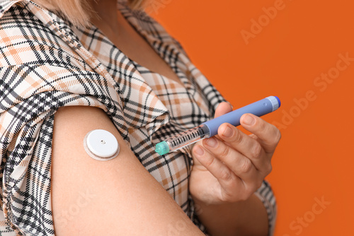 Woman with glucose sensor and lancet pen on orange background, closeup. Diabetes concept