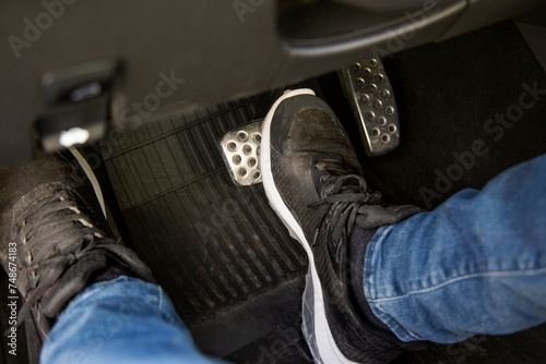 man's feet in black sneakers on the floor in a car pushing down the brake pedal, carefully driving car, waiting on the traffic light concept