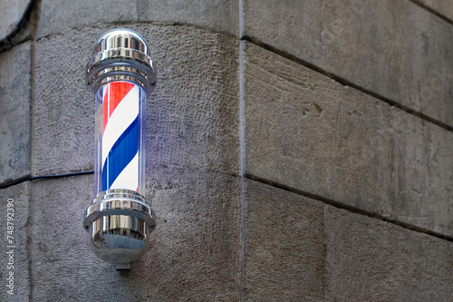 A classic barber pole with illuminated red, white and blue stripes, mounted on a stone wall on a street in Barcelona in Catalonia Spain