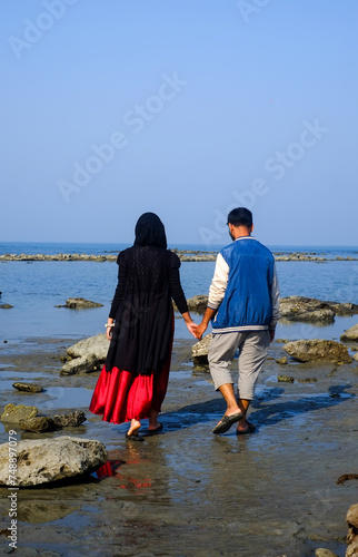 South asian young muslim couple walking in a sea beach holding their hands together 