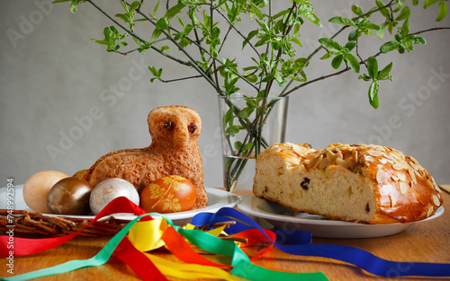 Easter still life containing a small lamb cake, painted eggs, traditional Czech Easter sweet cake called "mazanec", an Easter whip and green twigs in a vase