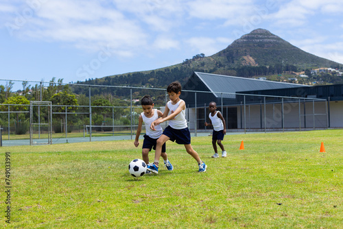 Biracial and African American children play soccer on a grassy field in school