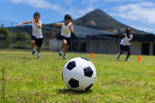 A soccer ball in focus with three children running behind it in school