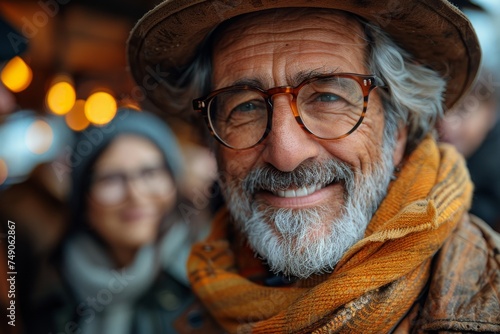 Portrait of an elderly man with a gray beard, wearing glasses and an orange scarf, looking at the camera