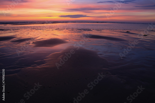 sunset sky is reflecting in the low tide draining waters of a beach in Sylt Island, Germany